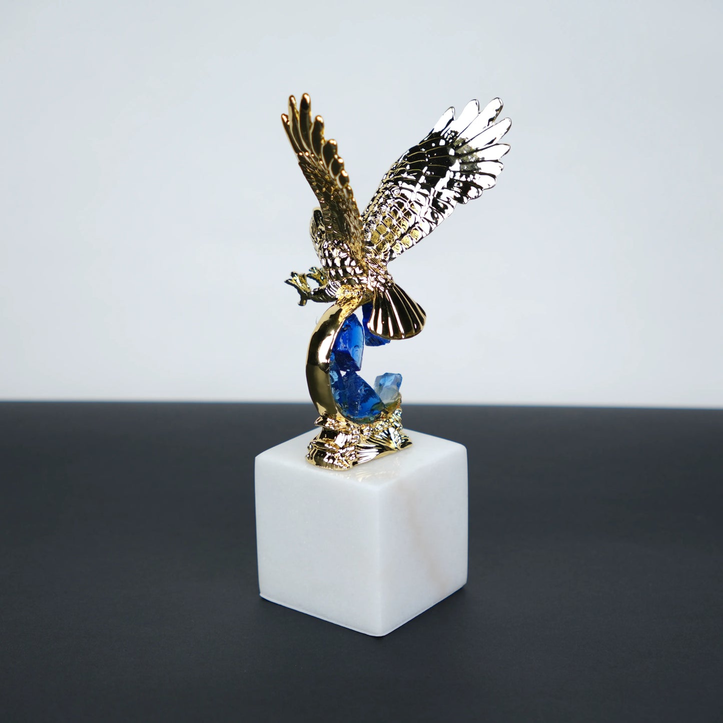 Golden eagle rising from blue crystal wave sculpture on white marble base