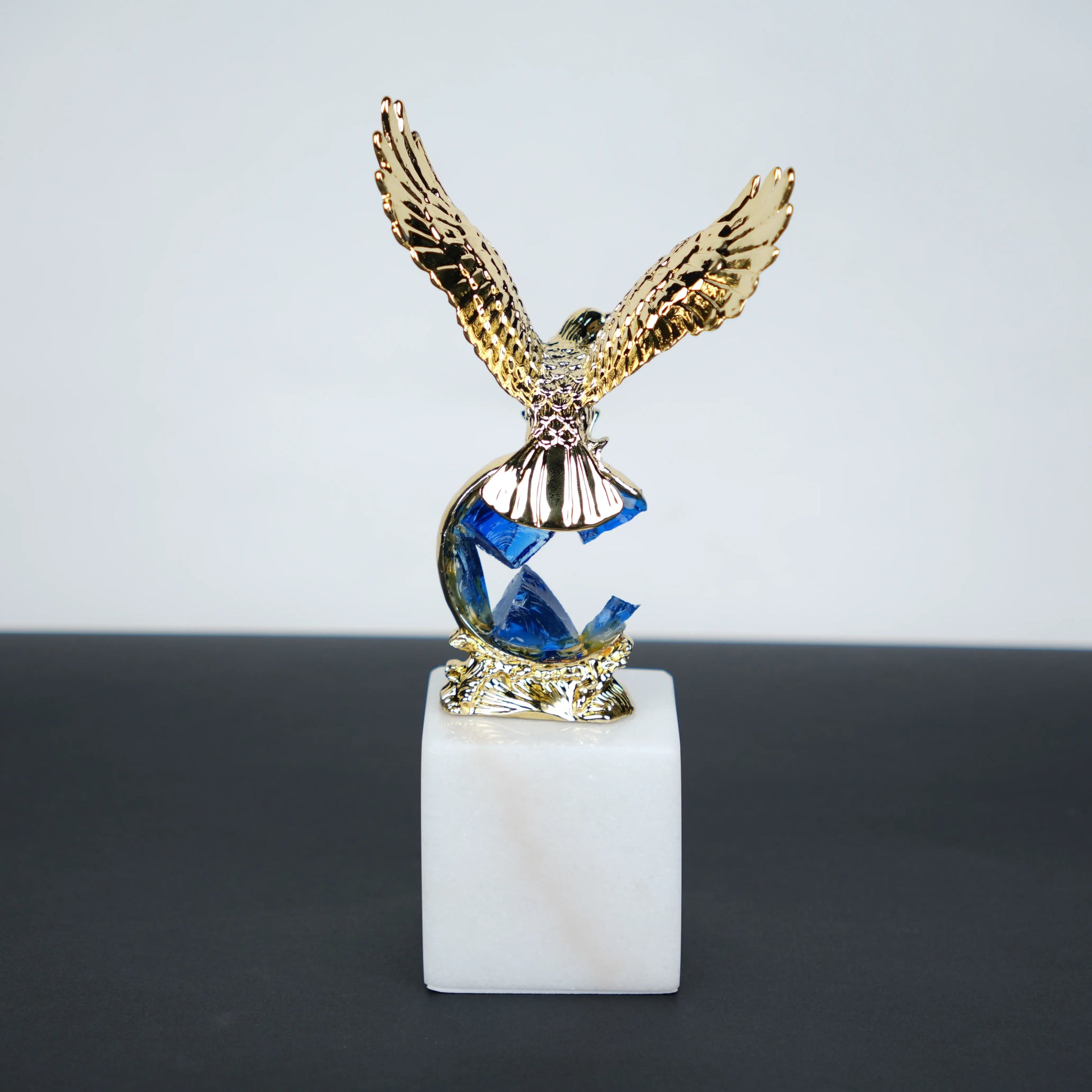 Golden eagle rising from blue crystal wave sculpture on white marble base