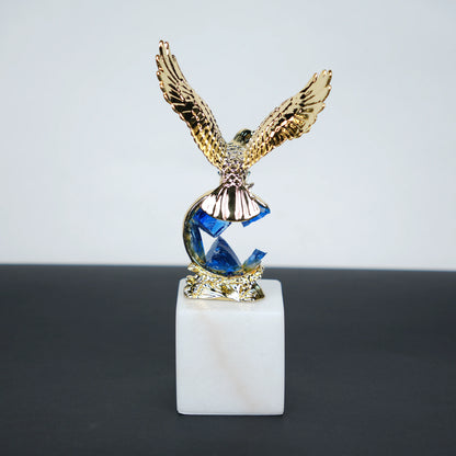 Golden eagle rising from blue crystal wave sculpture on white marble base