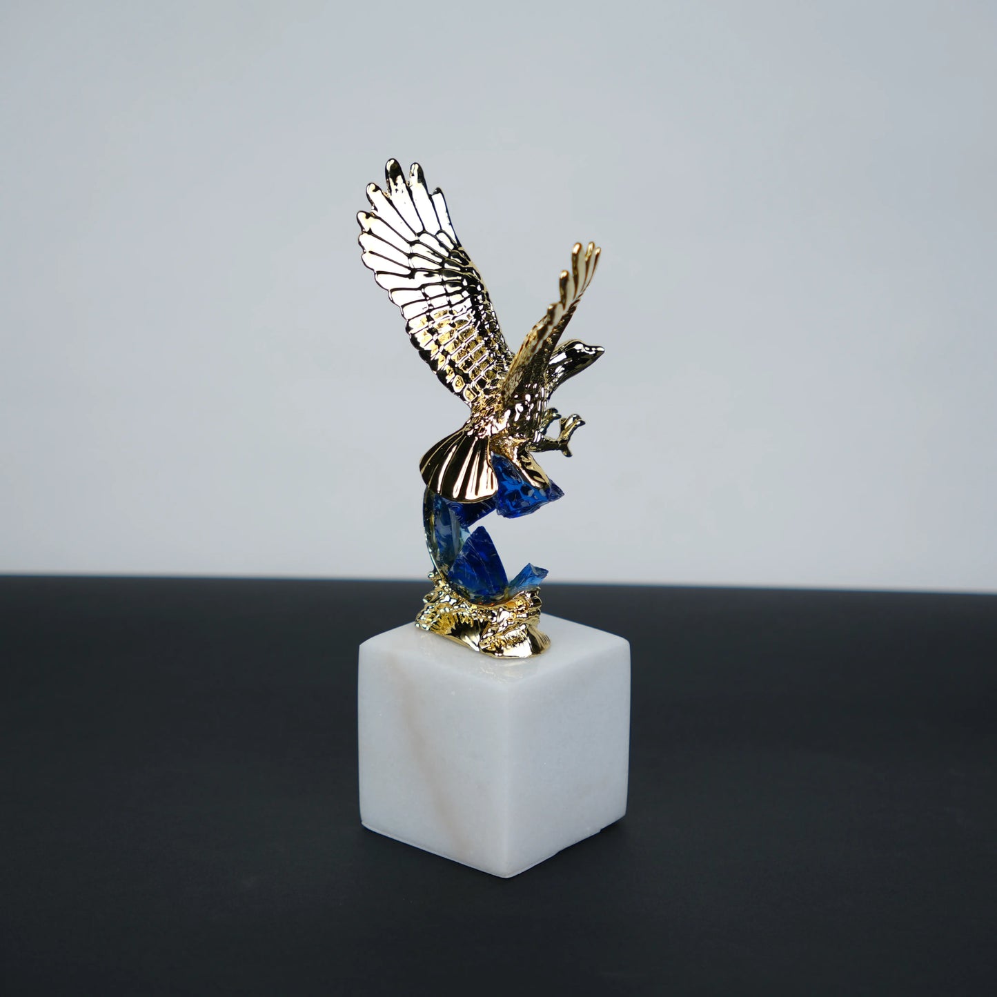 Golden eagle rising from blue crystal wave sculpture on white marble base