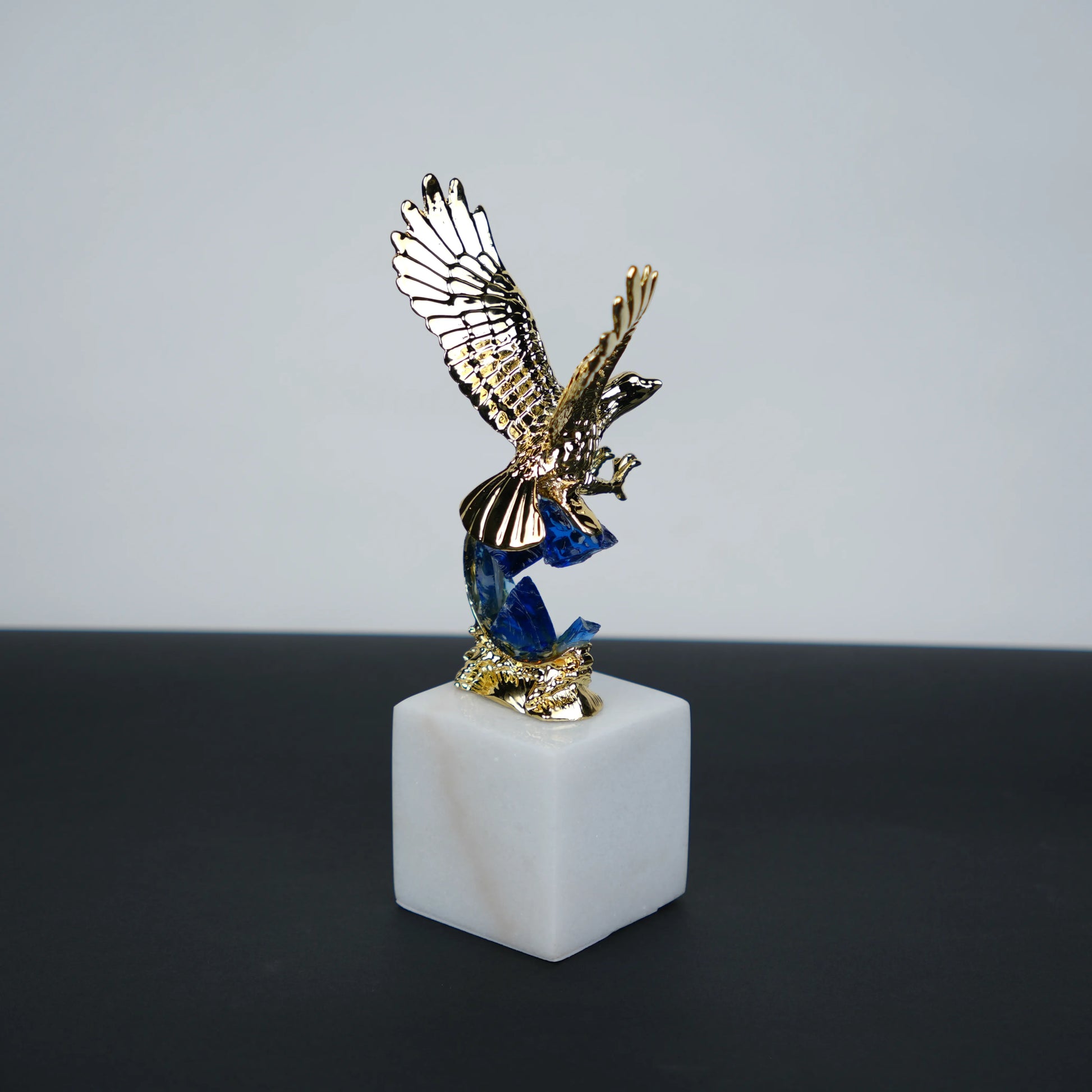 Golden eagle rising from blue crystal wave sculpture on white marble base