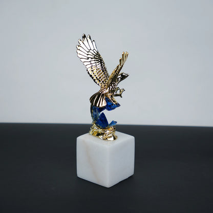 Golden eagle rising from blue crystal wave sculpture on white marble base