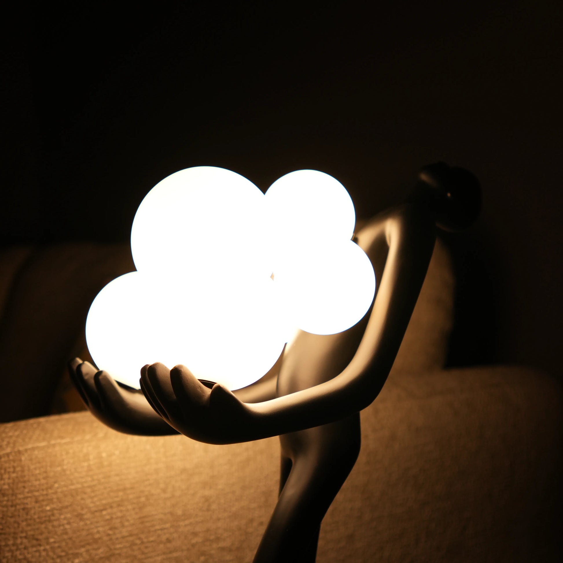 Black abstract human sculpture floor lamp holding glowing cloud-shaped warm white globes