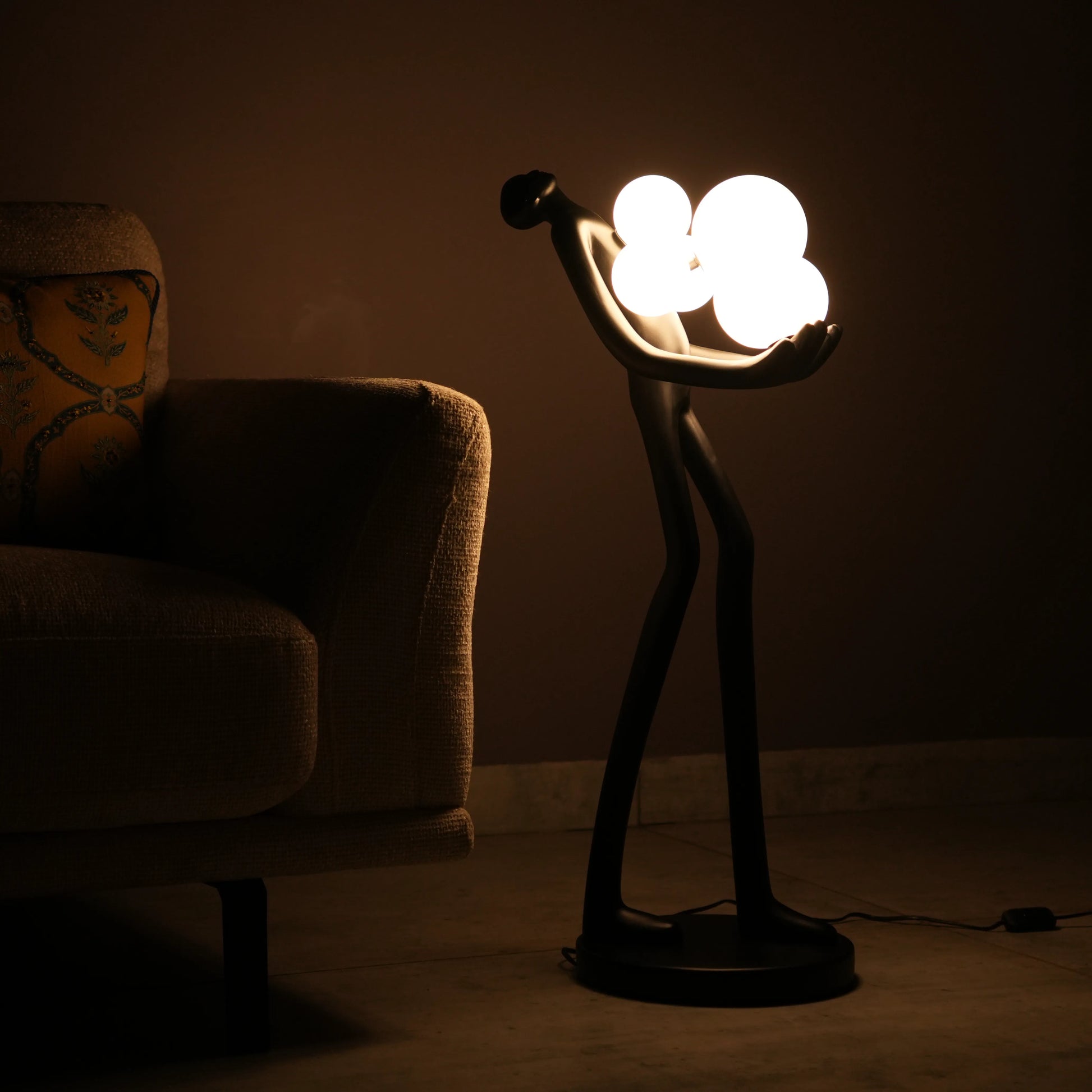 Black abstract human sculpture floor lamp holding glowing cloud-shaped warm white globes