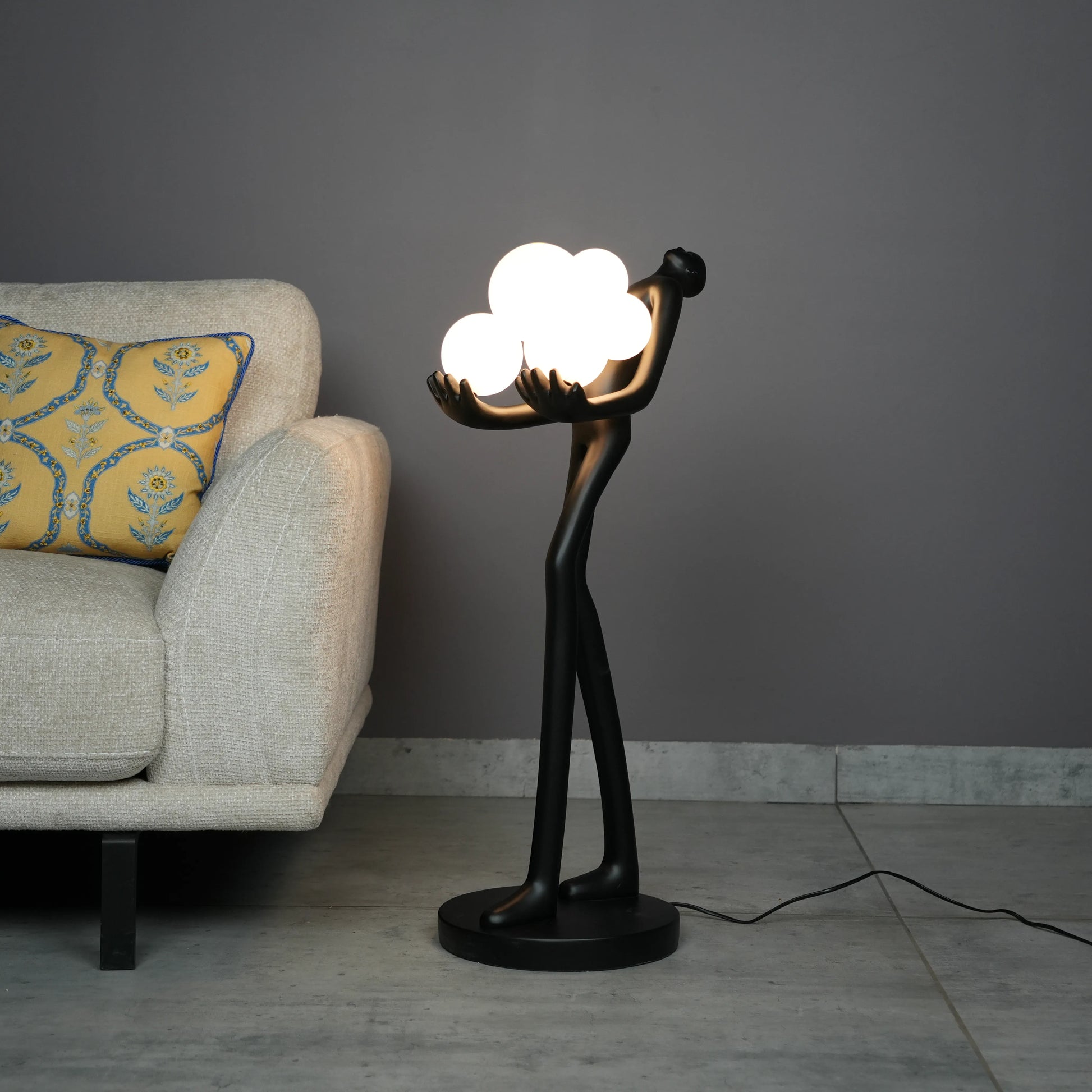 Black abstract human sculpture floor lamp holding glowing cloud-shaped warm white globes