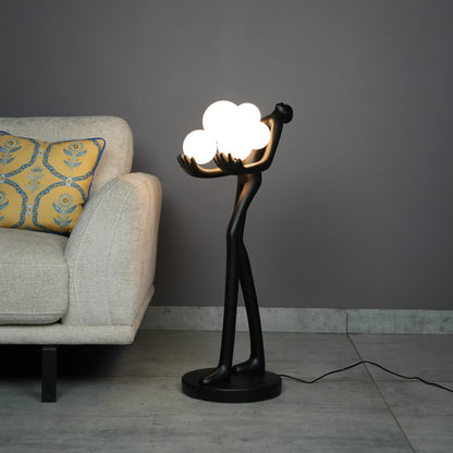 Black abstract human sculpture floor lamp holding glowing cloud-shaped warm white globes