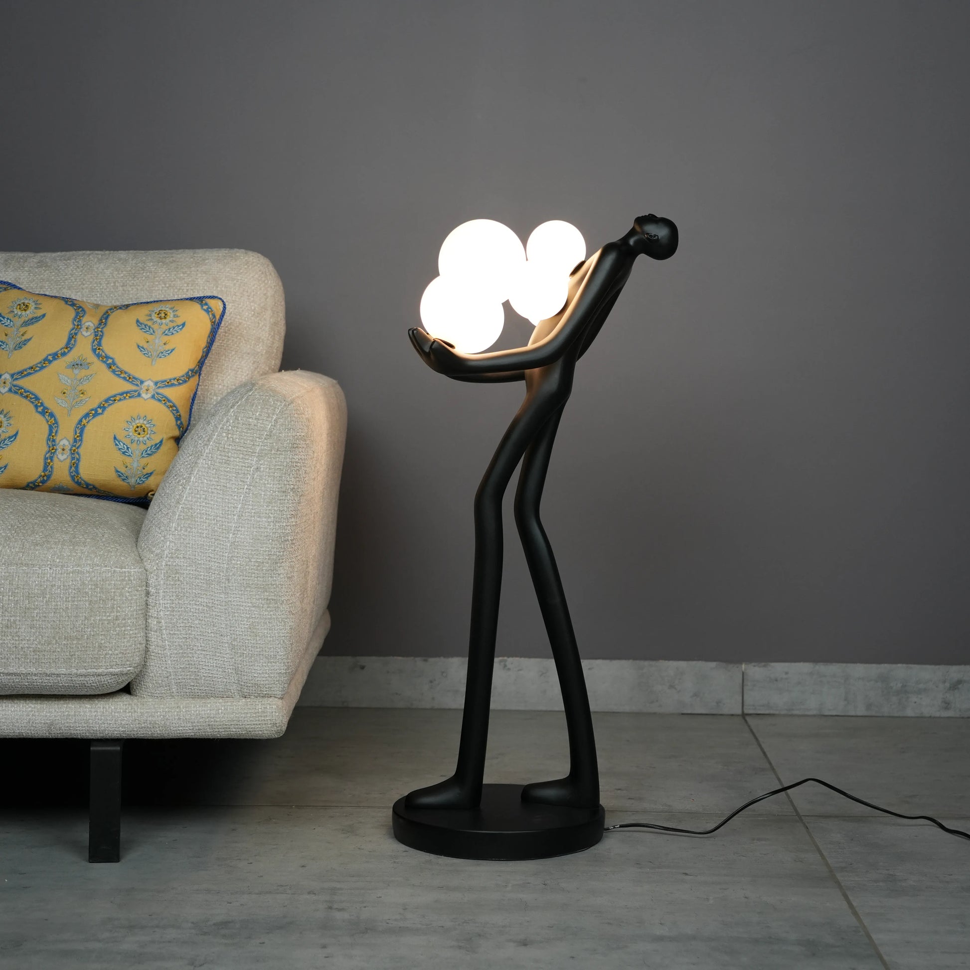 Black abstract human sculpture floor lamp holding glowing cloud-shaped warm white globes
