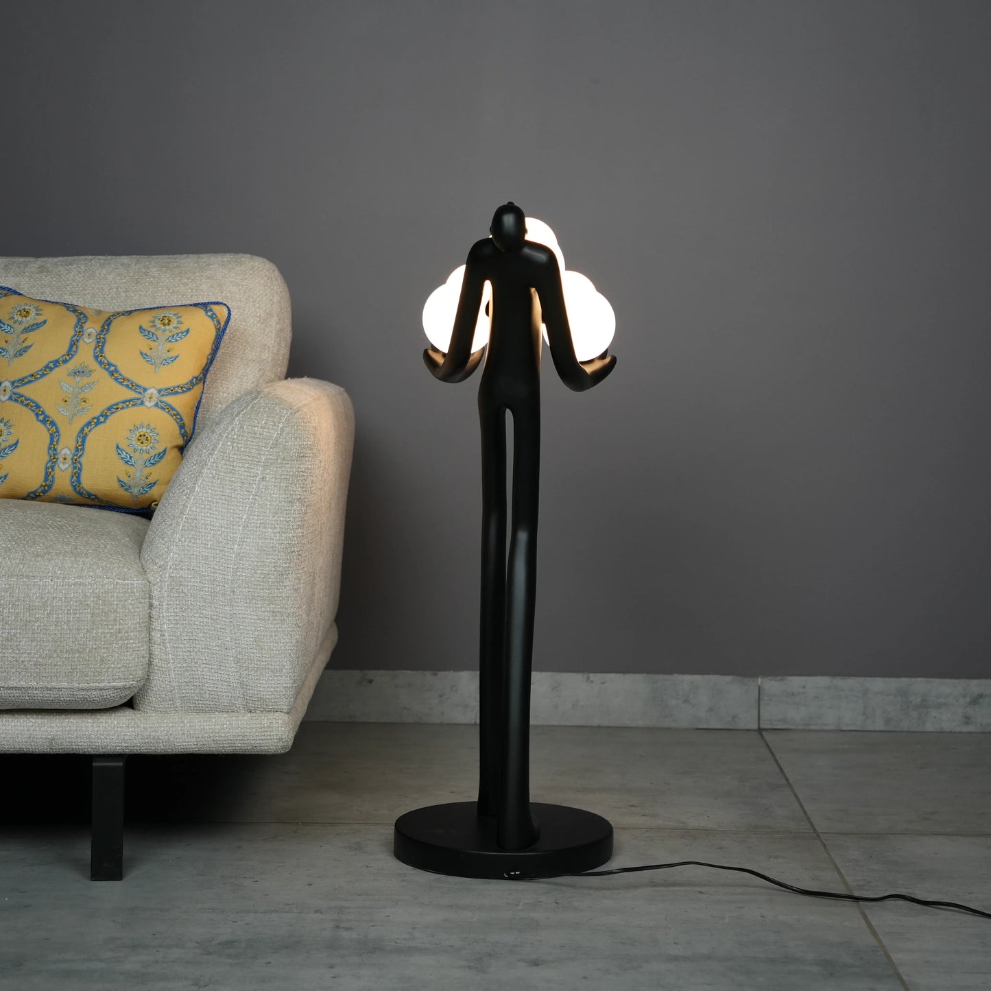Black abstract human sculpture floor lamp holding glowing cloud-shaped warm white globes