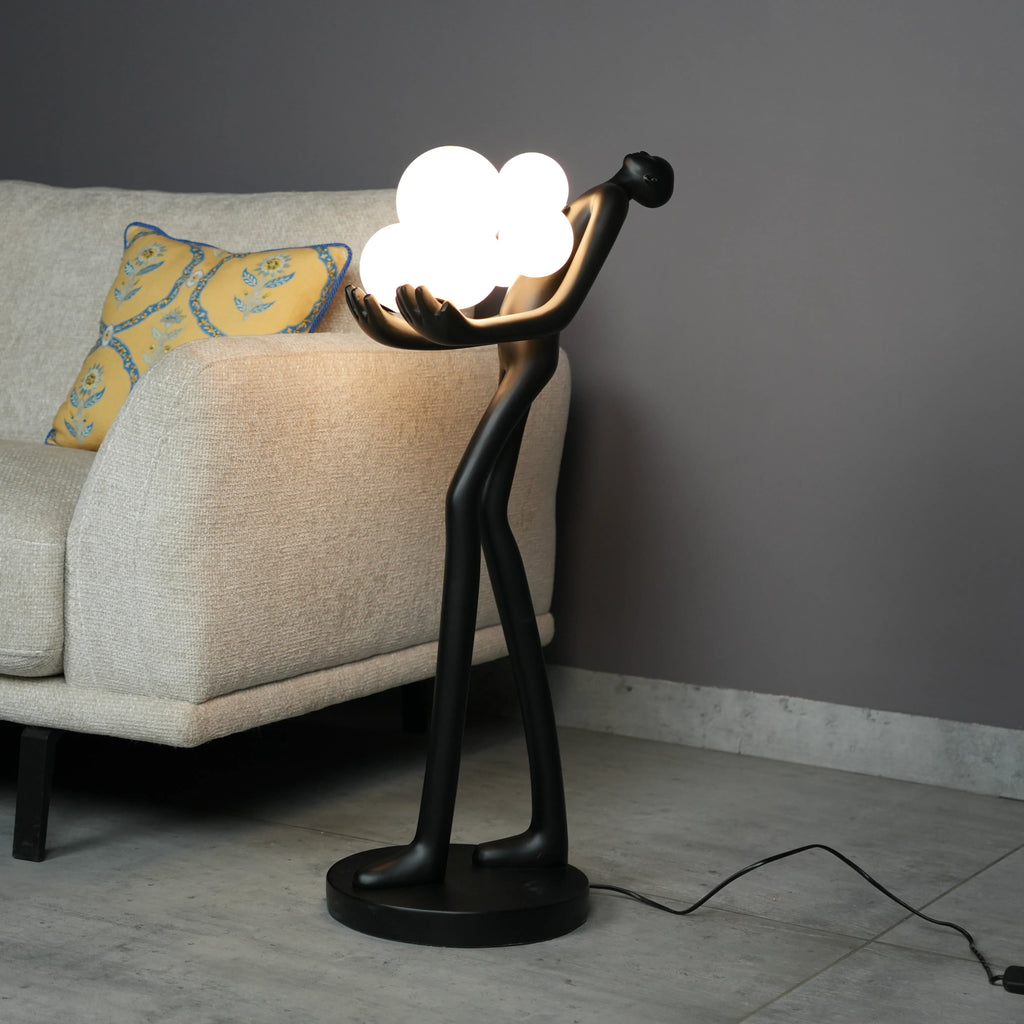 Luxury sculptural floor lamp with abstract human figure holding glowing orb lights in modern artistic black finish