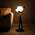 Black abstract human sculpture floor lamp holding glowing cloud-shaped warm white globes