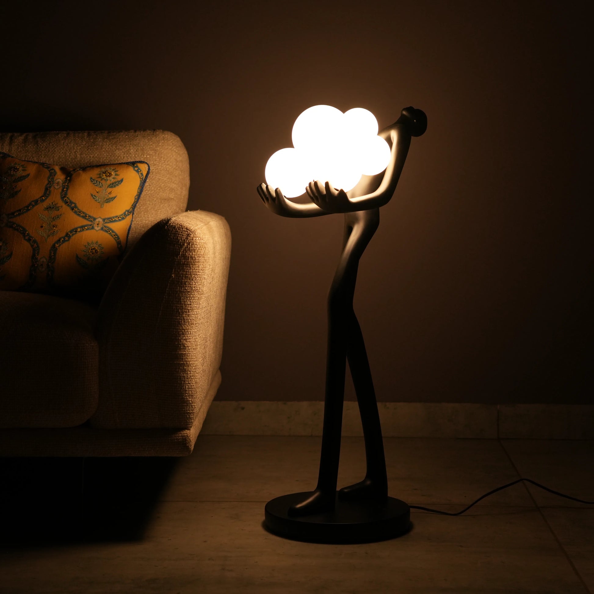Black abstract human sculpture floor lamp holding glowing cloud-shaped warm white globes