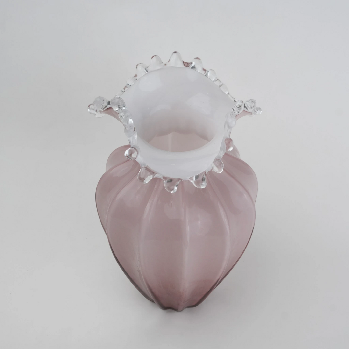 Blush pink translucent glass vase with curved body and sculptural ruffled rim.