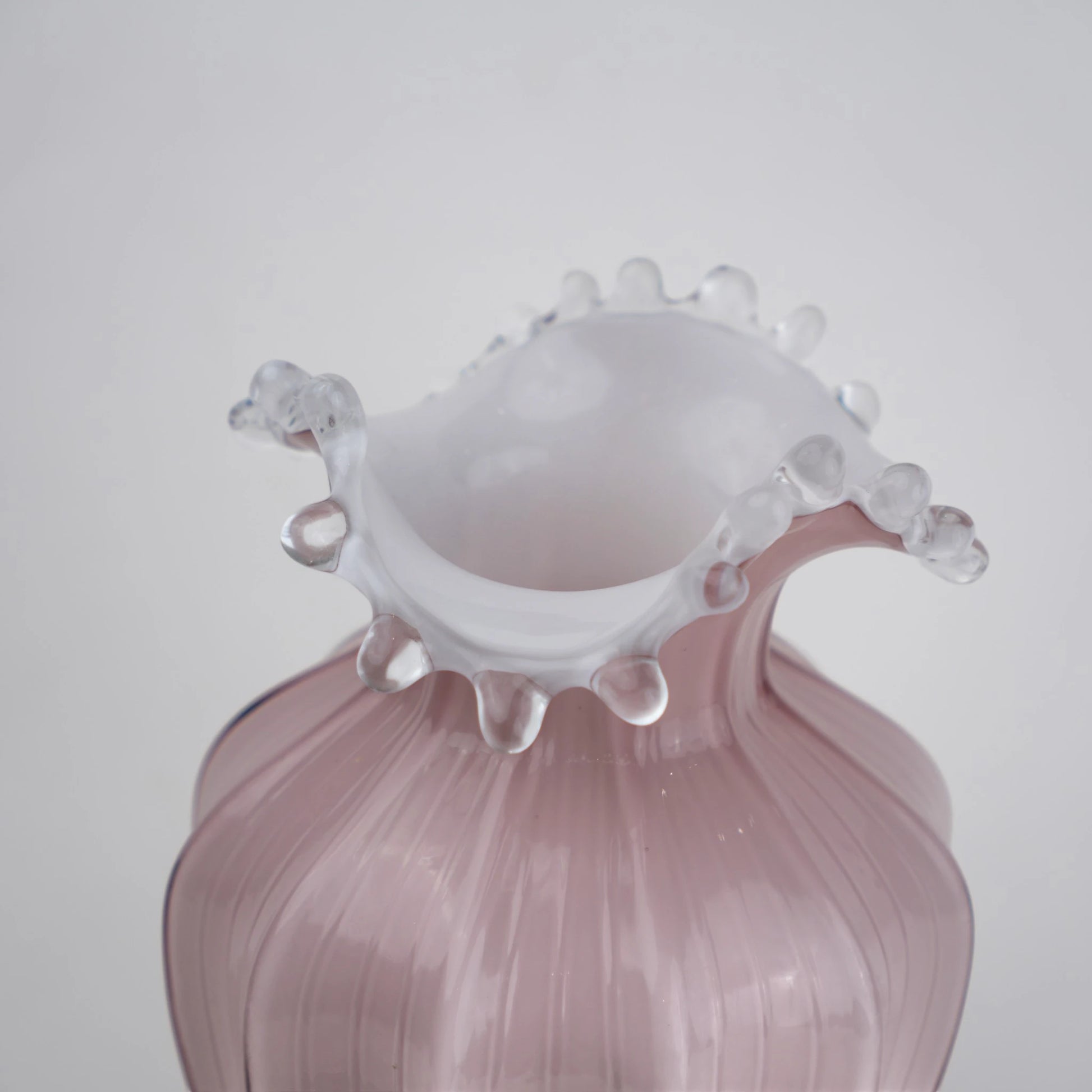 Blush pink translucent glass vase with curved body and sculptural ruffled rim.