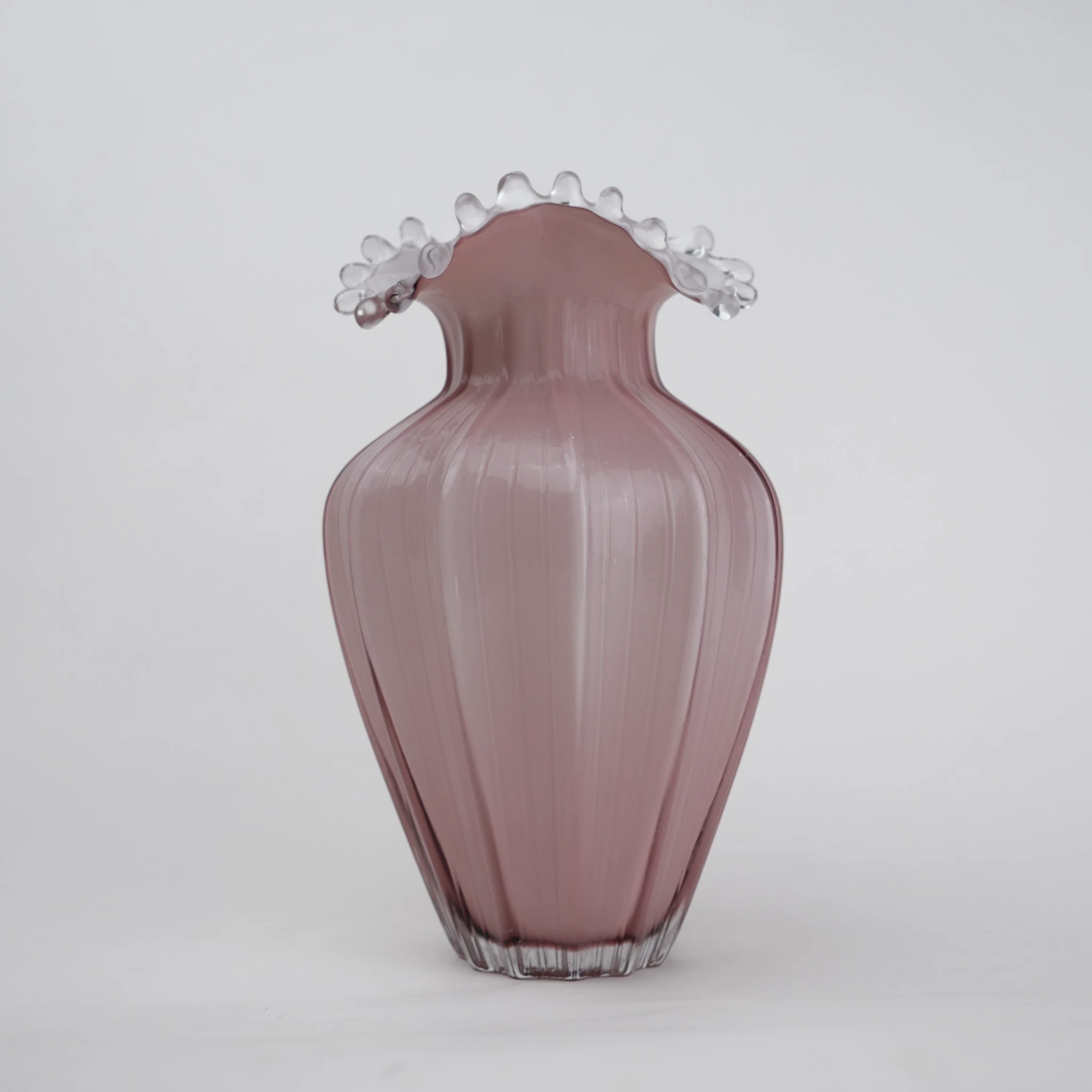 Blush pink translucent glass vase with curved body and sculptural ruffled rim.