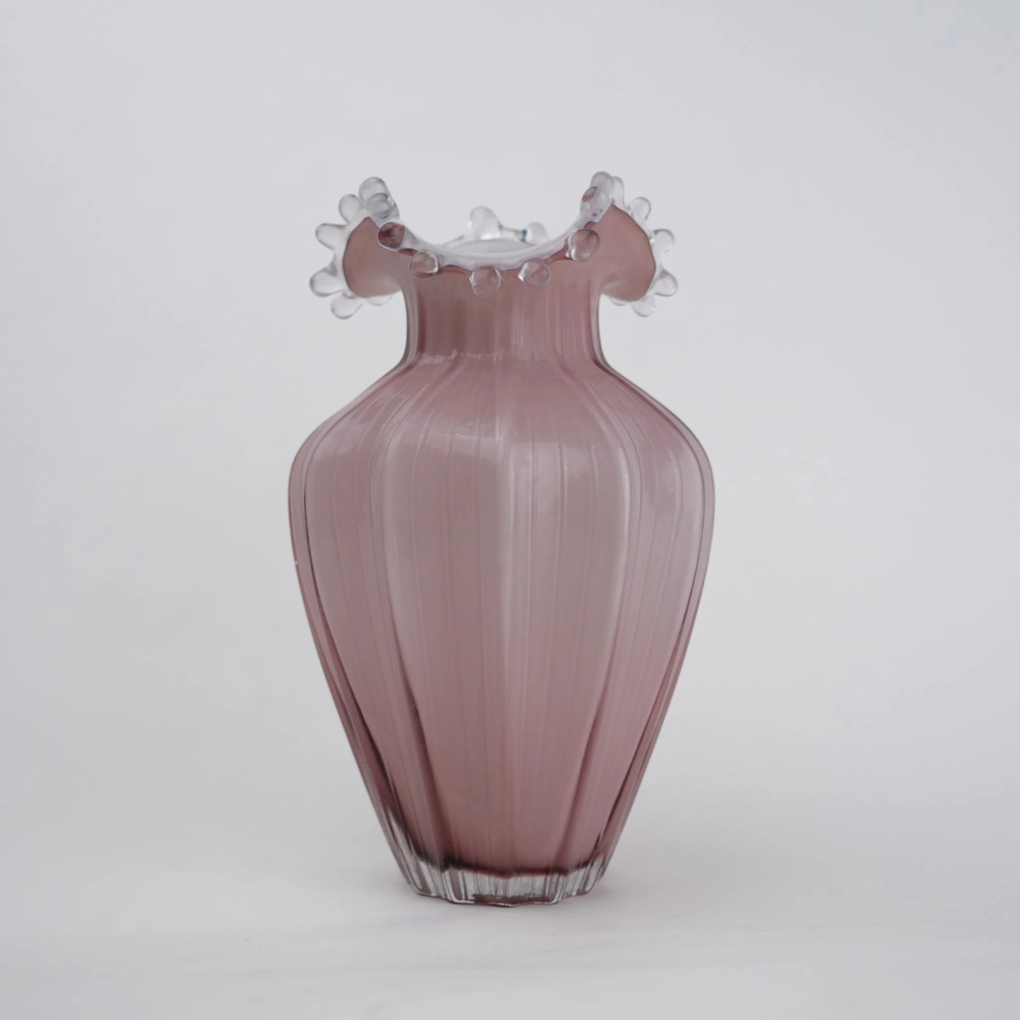 Blush pink translucent glass vase with curved body and sculptural ruffled rim.