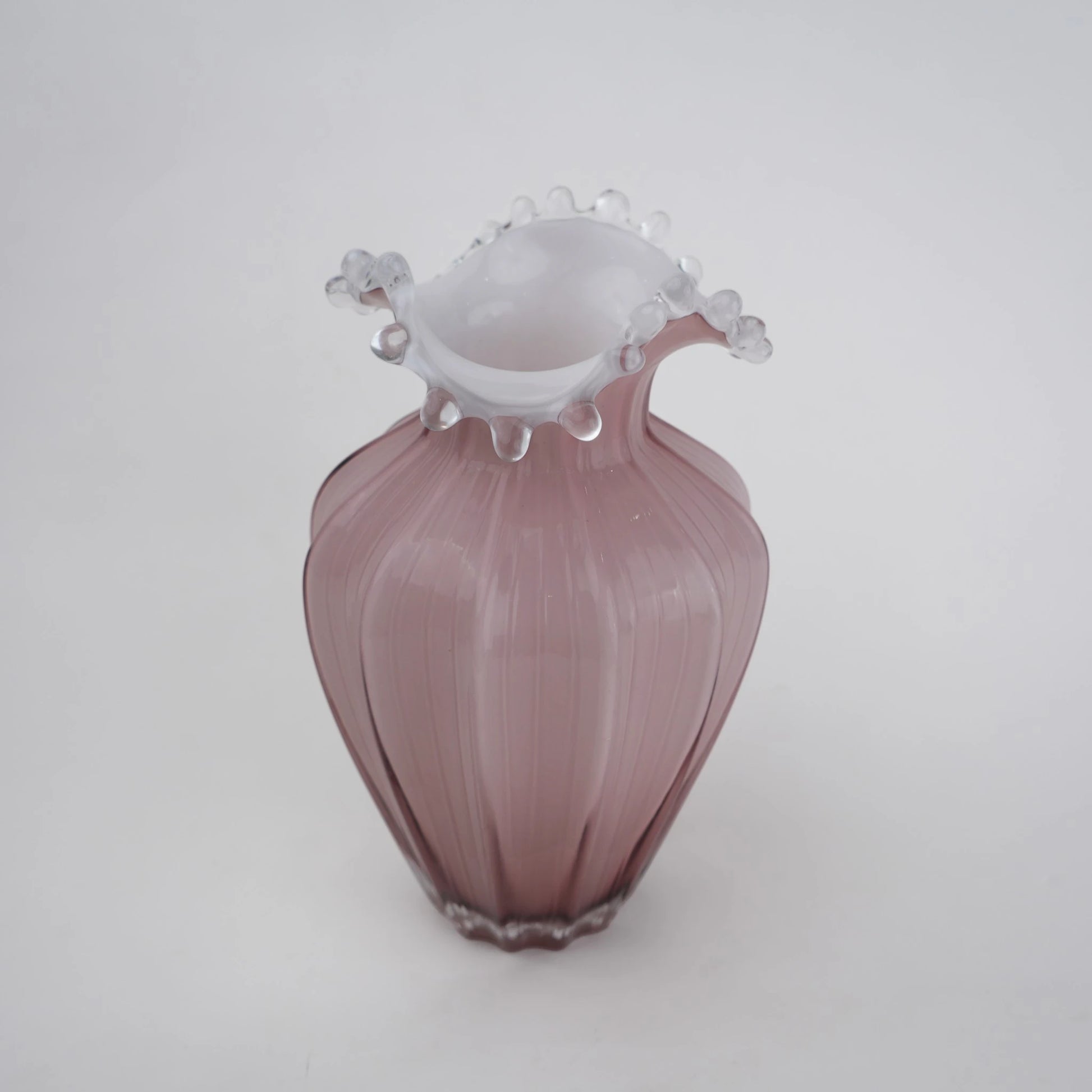 Blush pink translucent glass vase with curved body and sculptural ruffled rim.