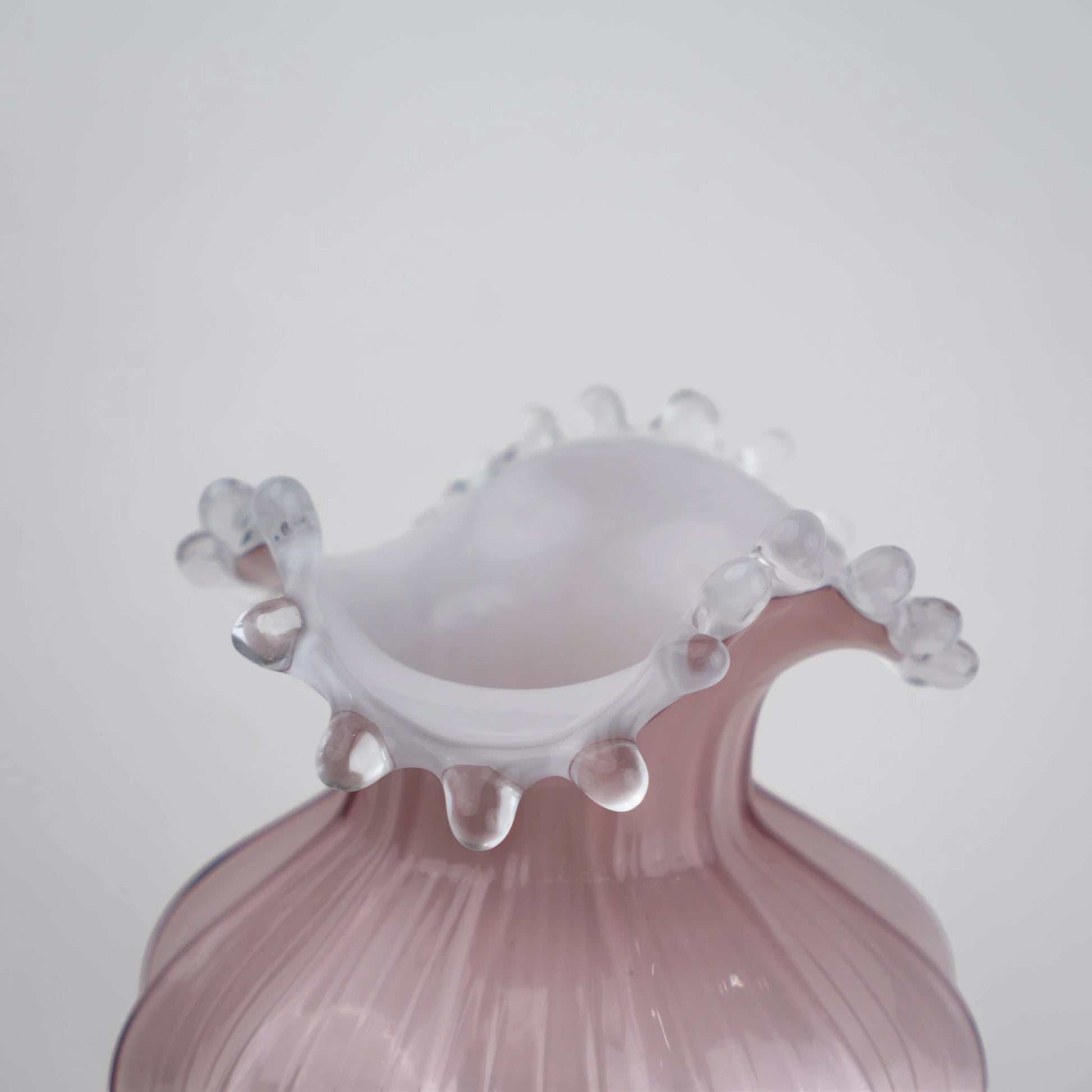 Blush pink translucent glass vase with curved body and sculptural ruffled rim.