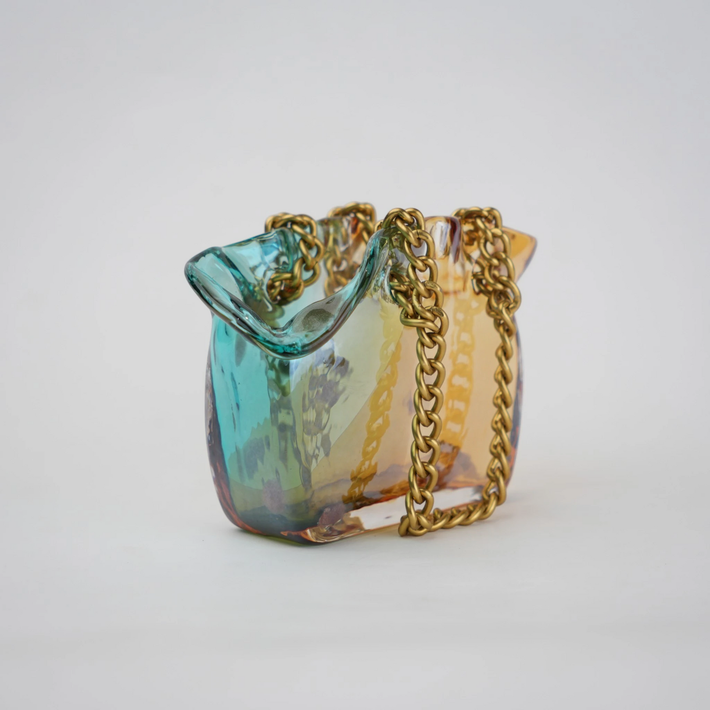 Dual-tone teal and amber glass vase with bubble texture, sculptural form, and metallic chain handle.