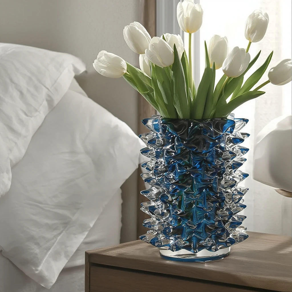 Blue and clear glass vase with white tulips on a bedside table.