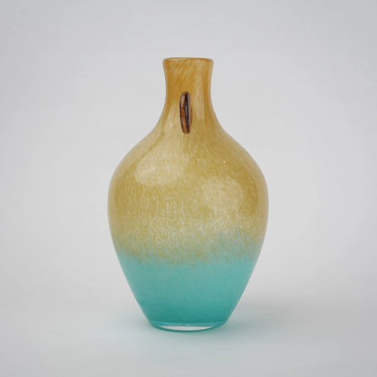 Ombre glass vase with a yellow to teal gradient finish, featuring a rounded body, narrow neck, and decorative side accents, designed as a modern artistic piece for home decor styling.