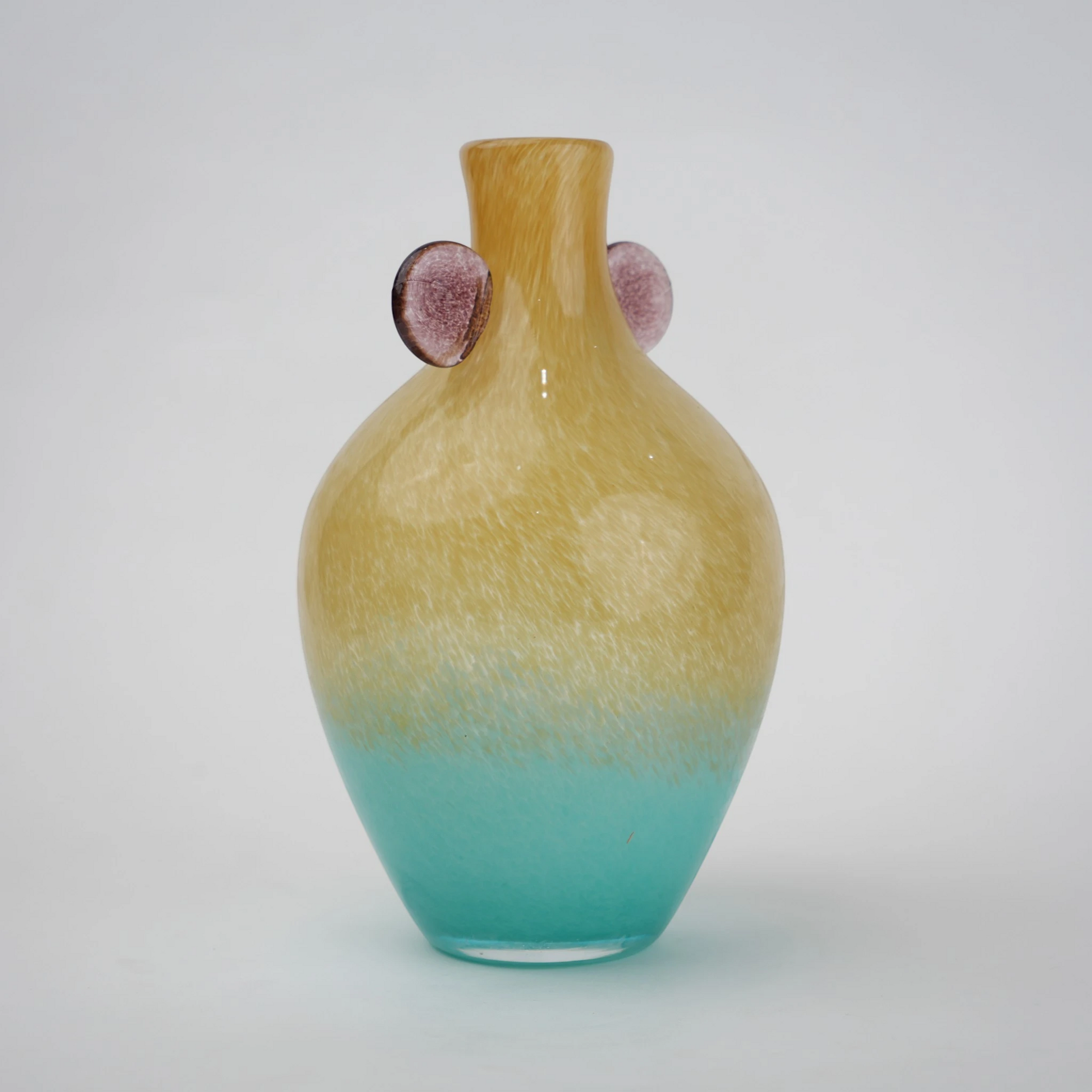 Ombre glass vase with a yellow to teal gradient finish, featuring a rounded body, narrow neck, and decorative side accents, designed as a modern artistic piece for home decor styling.