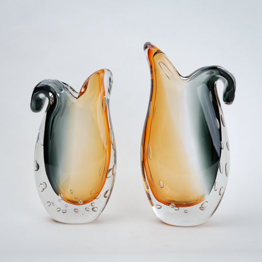 Two glass vases with a gradient color from orange to gray on a light gray background