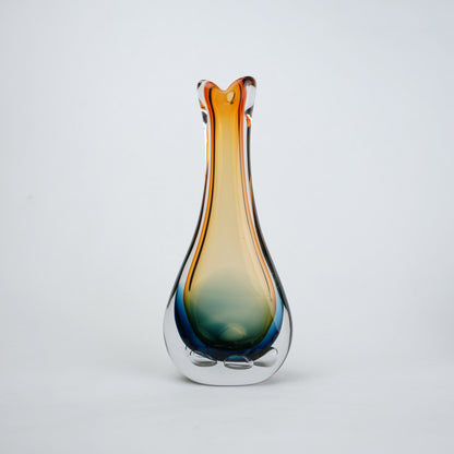 Glass vase with gradient color from blue to orange on a light gray background