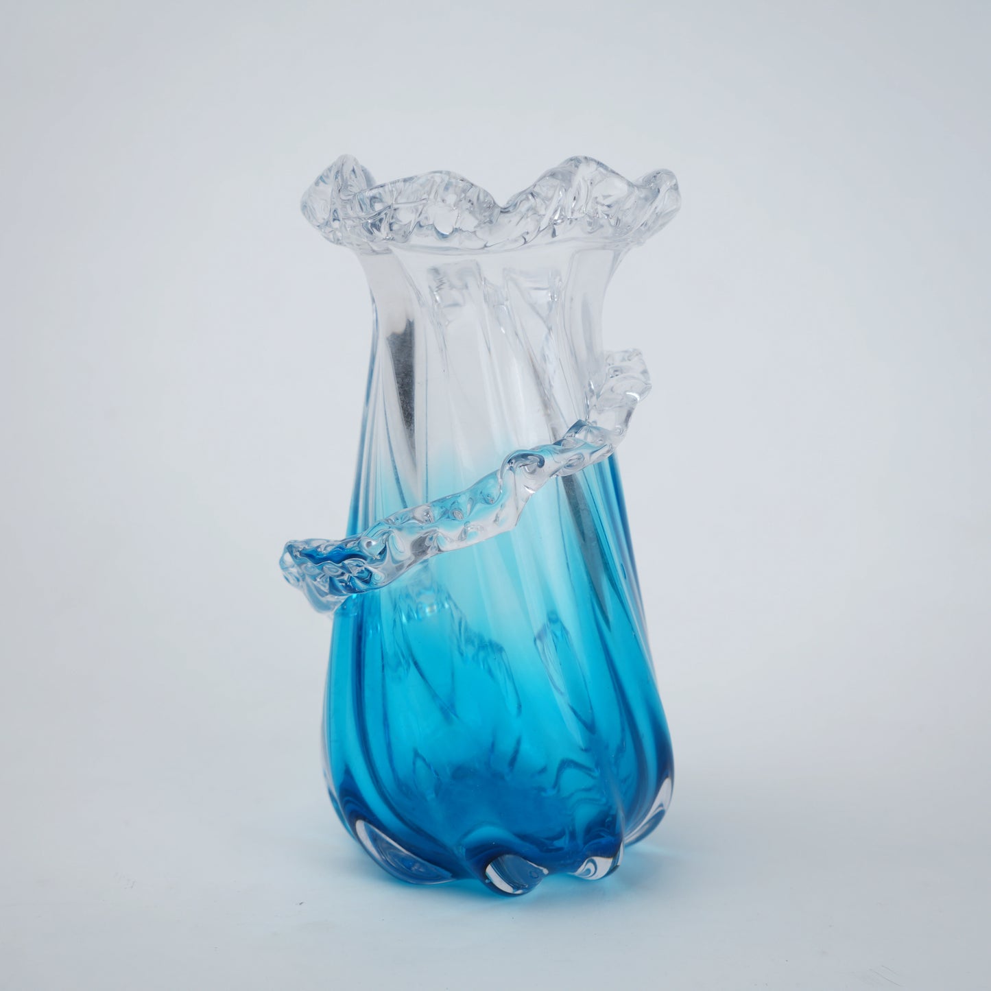 Glass vase with blue base and ruffled top on a light gray background