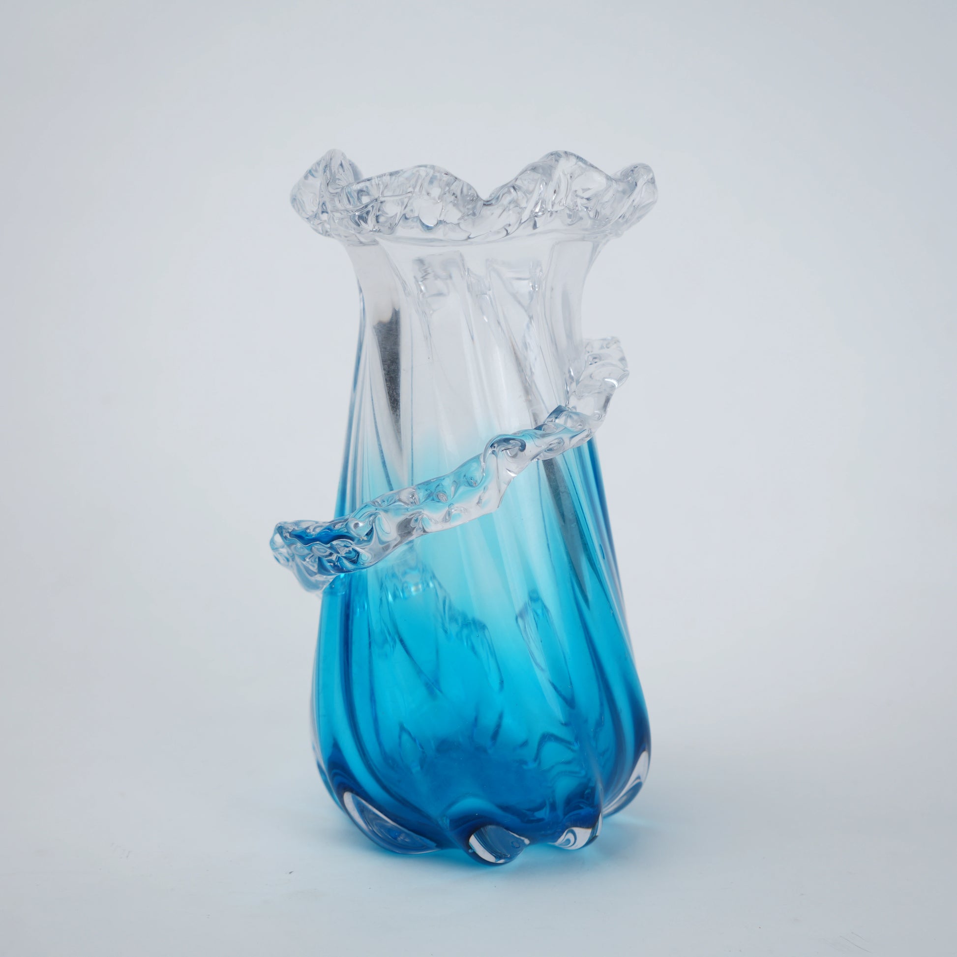 Glass vase with blue base and ruffled top on a light gray background