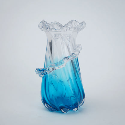 Glass vase with blue base and ruffled top on a light gray background