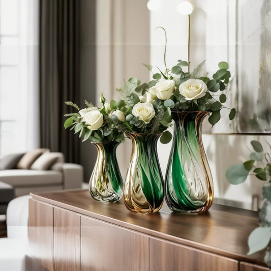 Three green and gold vases with flowers on a wooden cabinet in a living room.
