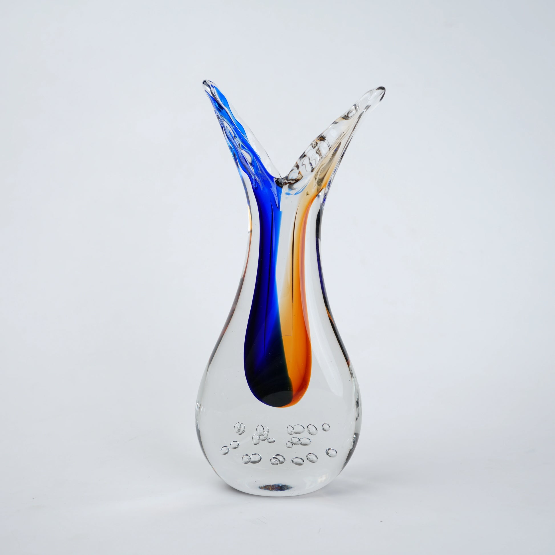 Clear glass decorative vase with asymmetrical flared opening featuring flowing blue and amber color streams inside and textured air bubble detailing at the base.