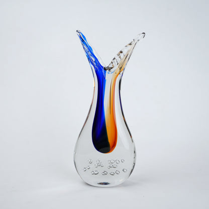 Clear glass decorative vase with asymmetrical flared opening featuring flowing blue and amber color streams inside and textured air bubble detailing at the base.