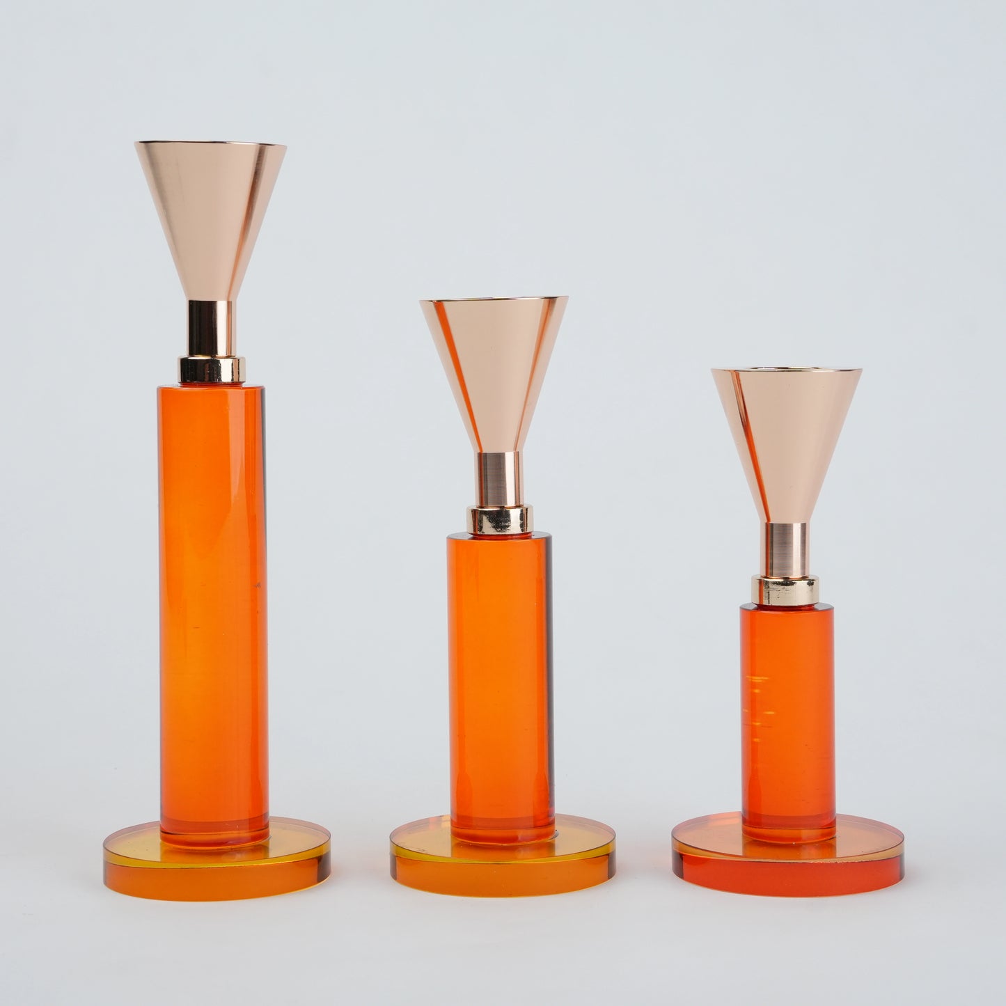 Three orange cylindrical objects with rose gold accents on a light gray background