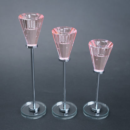 Three clear glass candle holders on stands against a dark background