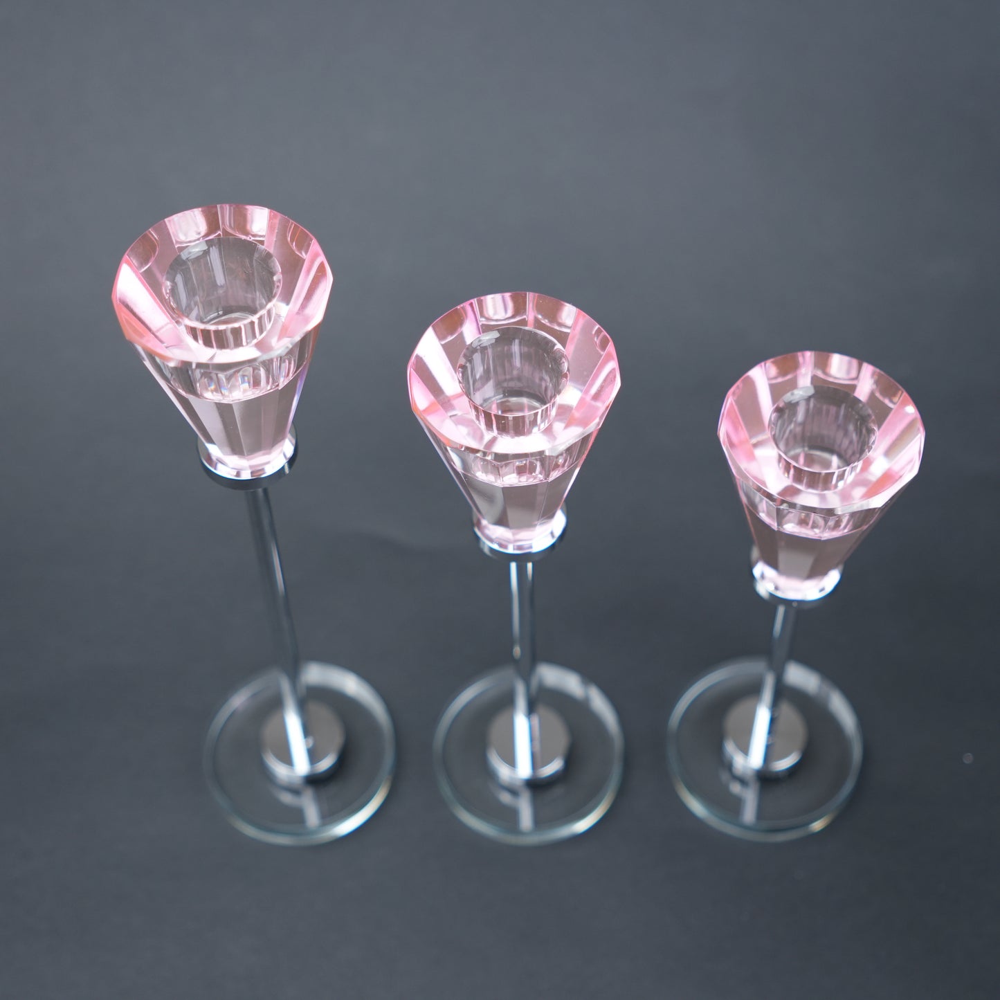 Three small pink crystal candle holders on a dark background
