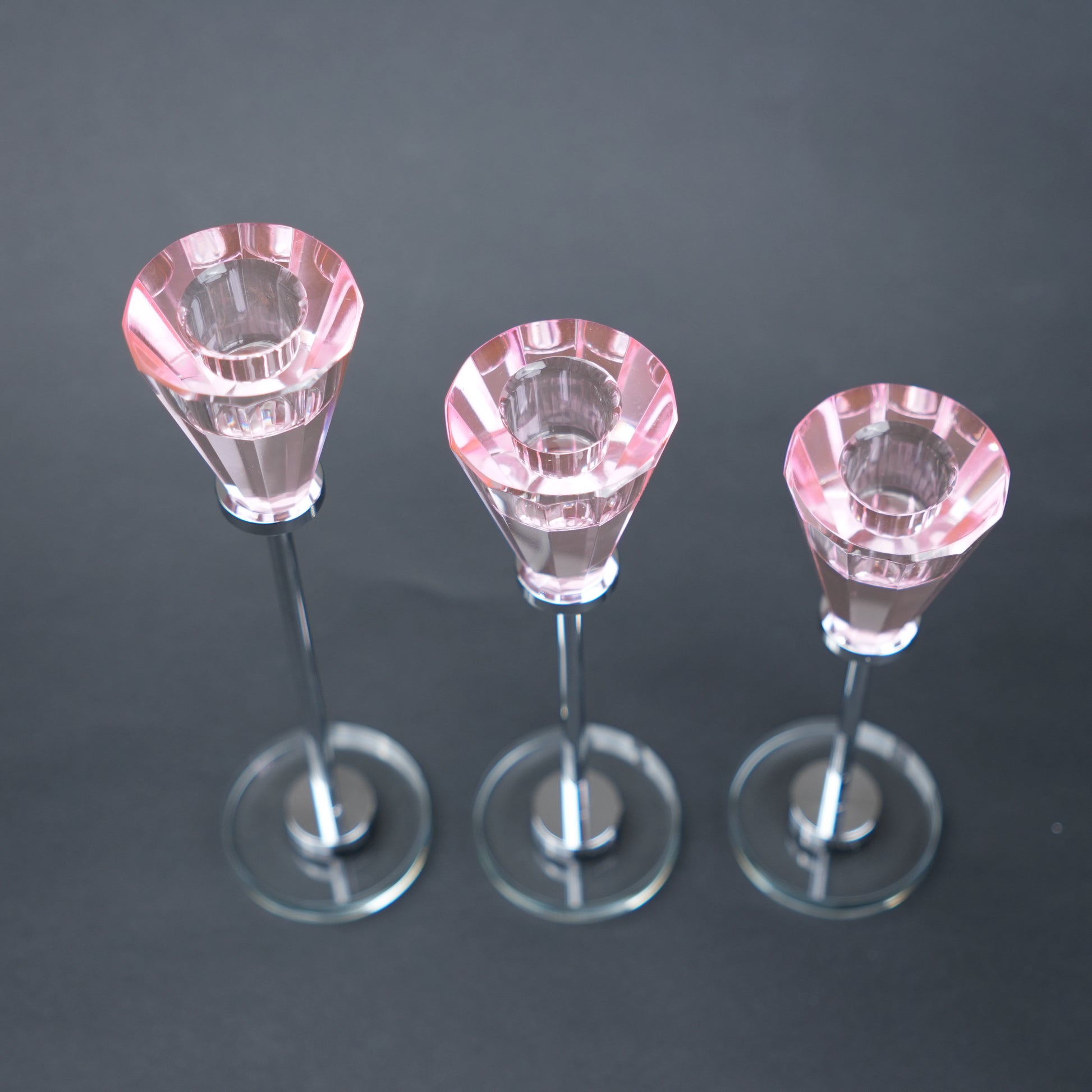 Three small pink crystal candle holders on a dark background