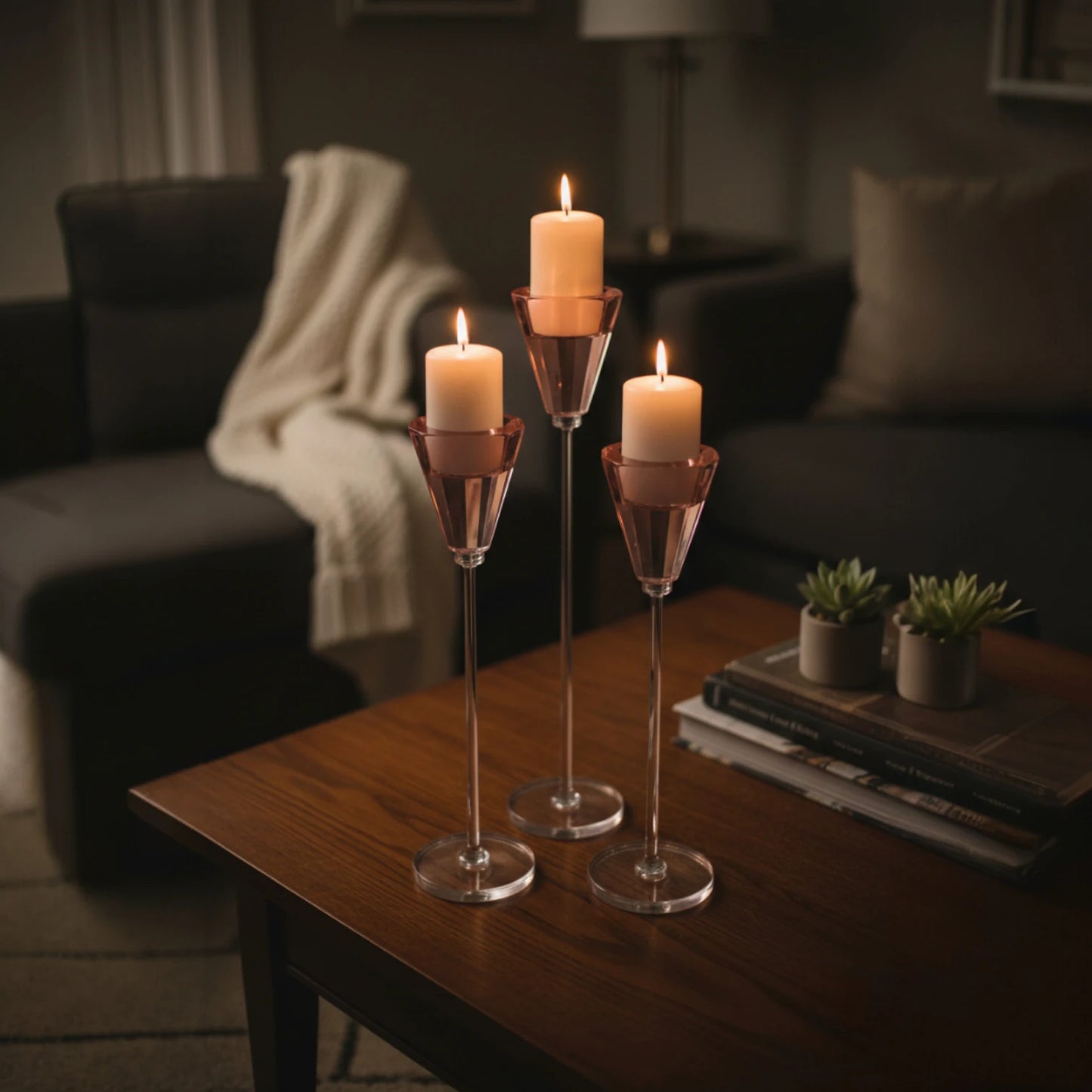 Three candles in glass holders on a wooden table in a dimly lit living room.