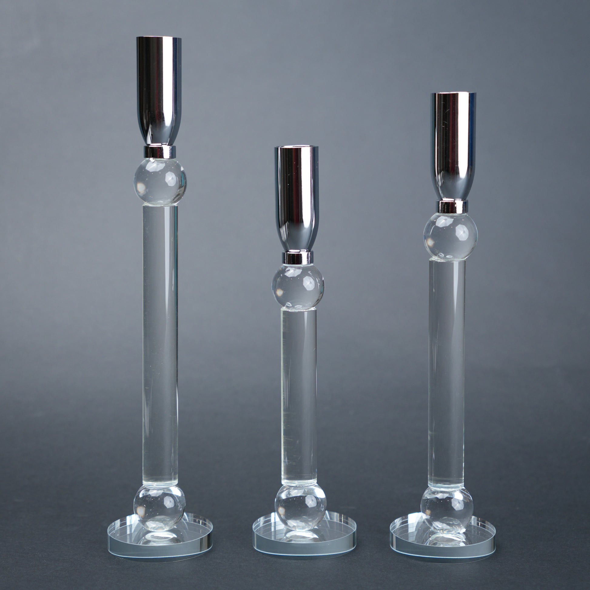 Three glass candle holders with silver bases on a gray background
