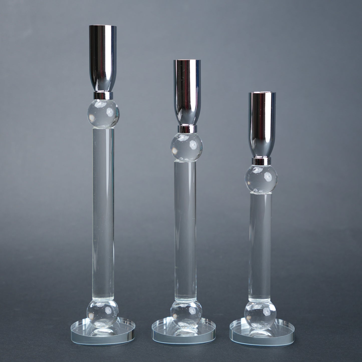 Three glass candle holders with silver bases on a gray background