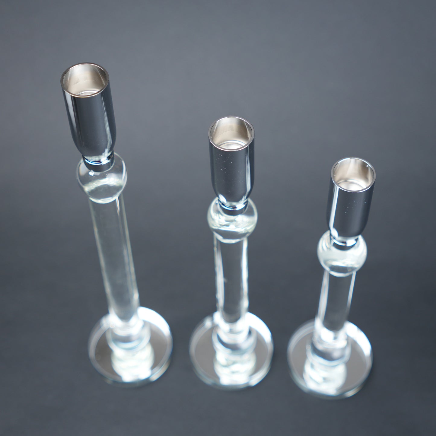 Three glass candle holders with silver bases on a dark background