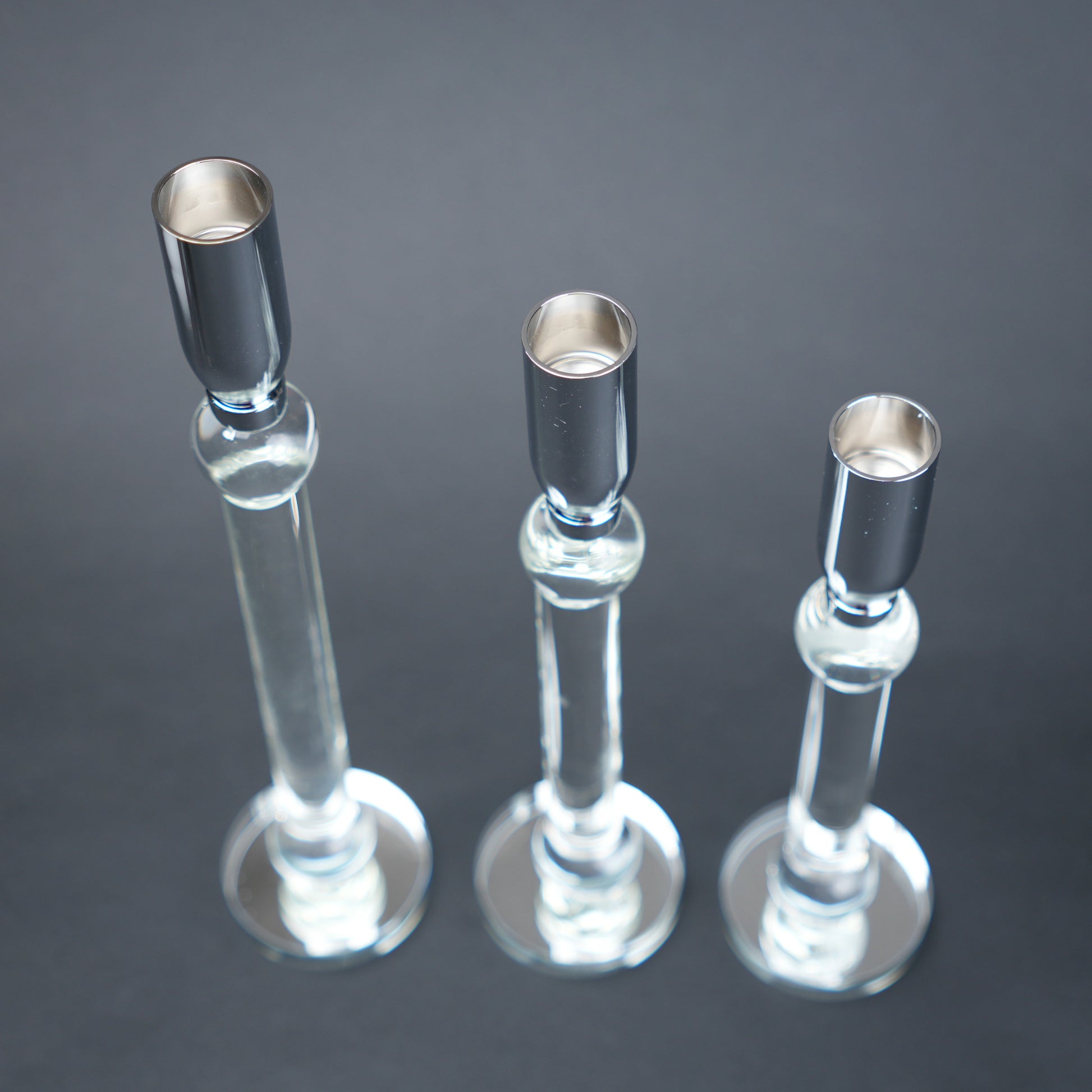 Three glass candle holders with silver bases on a dark background