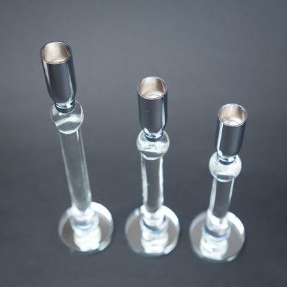 Three glass candle holders with silver bases on a dark background