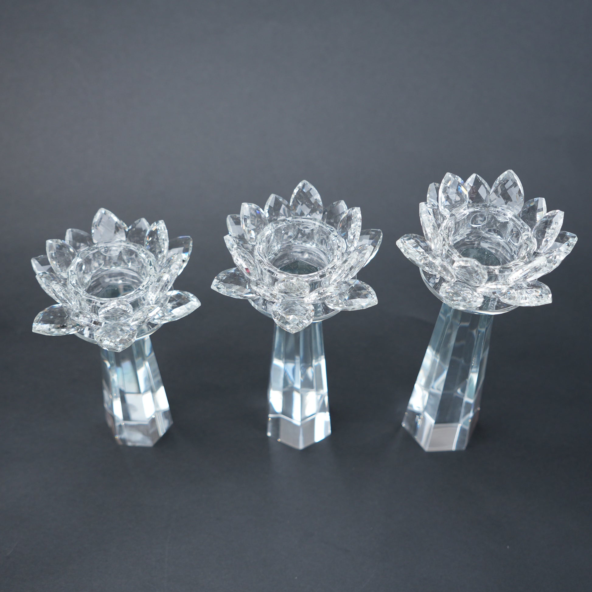Three clear glass lotus flower candle holders on a dark background
