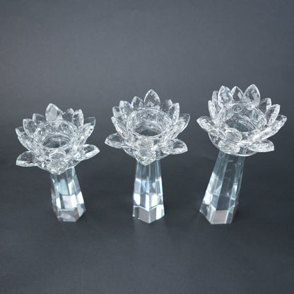 Three clear glass lotus flower candle holders on a dark background