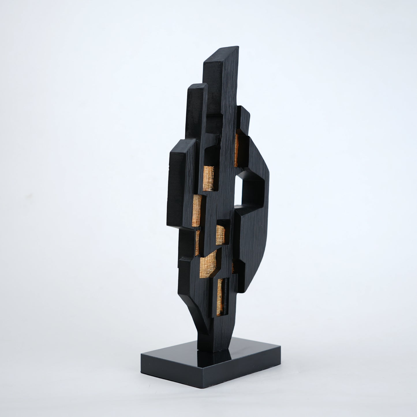 Abstract black decor object with geometric cut design and gold accents on base stand