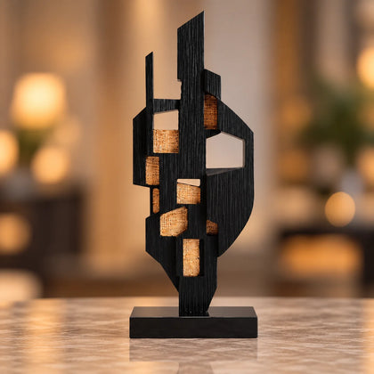 Abstract black decor object with geometric cut design and gold accents on base stand