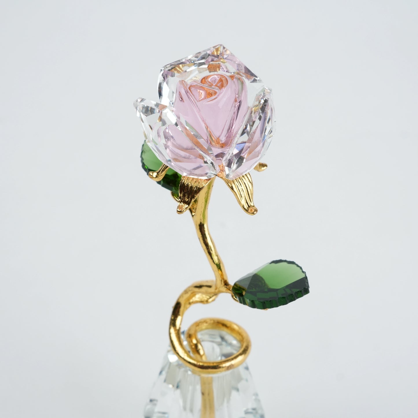 Crystal rose with gold stem and green leaves on a light gray background