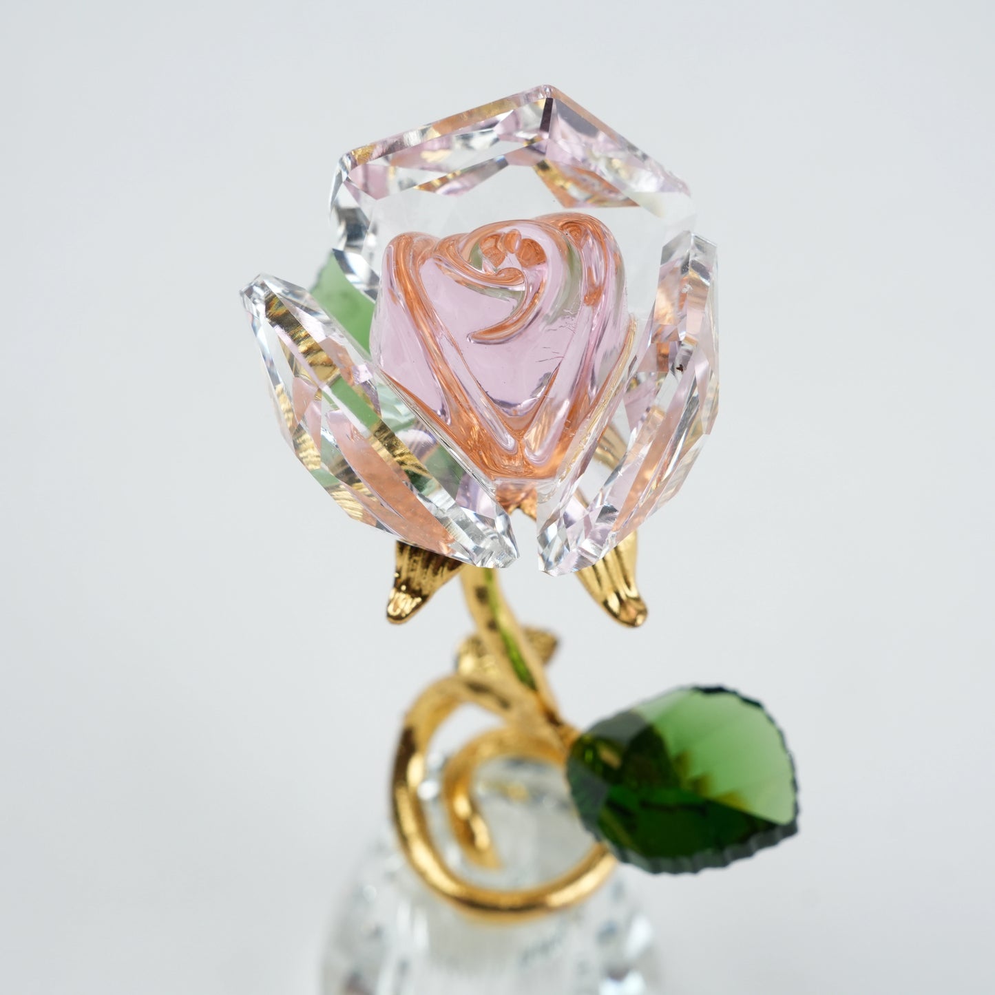 Crystal rose with green gemstone on a clear base against a light gray background