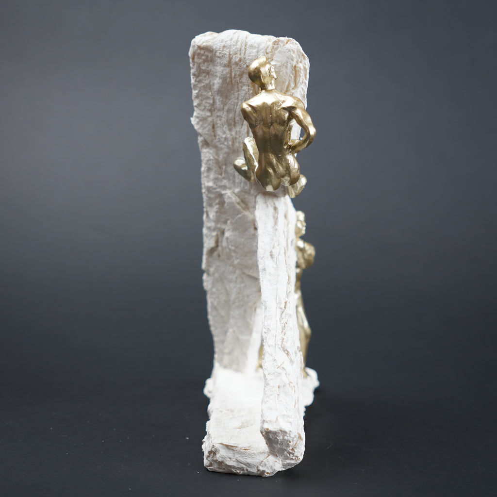 Gold figurine on a white rock-like structure against a dark background